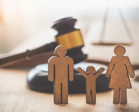 Wooden figures of a man, woman, and child stand in front of a gavel and a scale, symbolizing family law and justice.