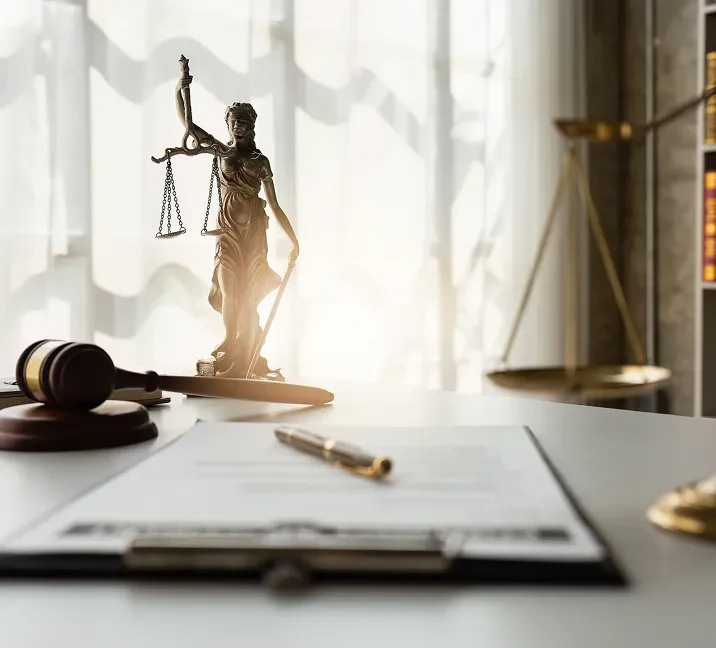 A gavel, legal documents, and a statue of Lady Justice with scales, set in a bright office environment.
