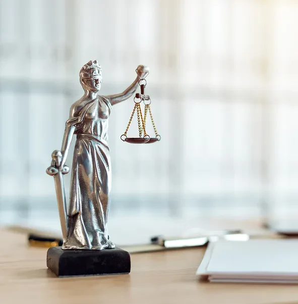A silver Lady Justice figurine holding scales and a sword, placed on a wooden surface with stationery in the background.