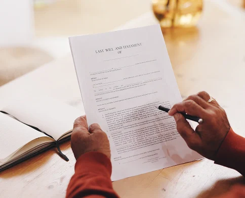 An individual reviews and signs a document titled Last Will and Testament with a pen in hand and an open book nearby.